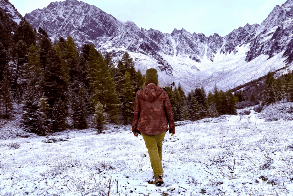 Wanderung im Herbst über eine schneebedeckte Wiese, im Hintergrund weiße Berge